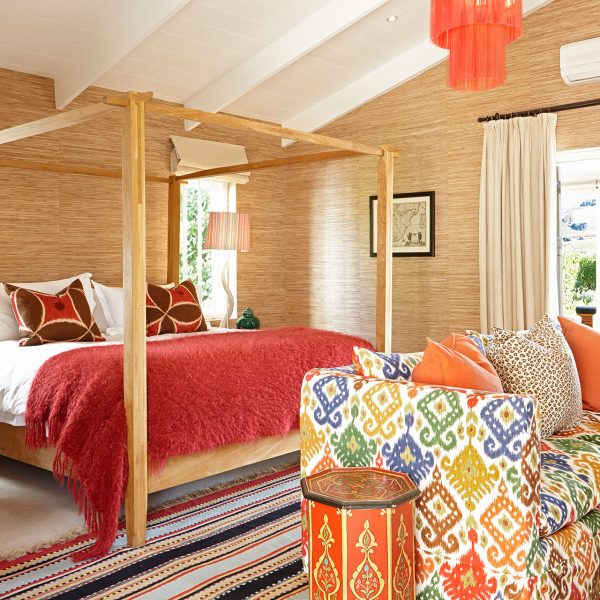 A four-poster bed in minimalistic style with bright red and orange design elements in the furniture and linen