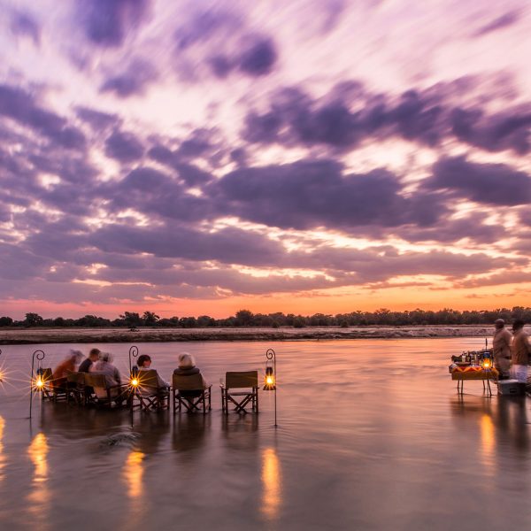 Guests enjoy a sundowner in the river as the sun sets