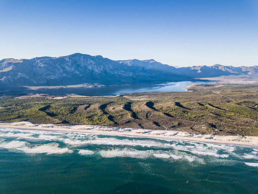 An aerial view from the ocean looking back at the sand dunes, lagoon and mountains around Walker Bay