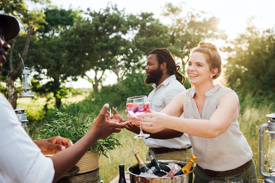 staff handing out sundowner drinks to guests on game drive