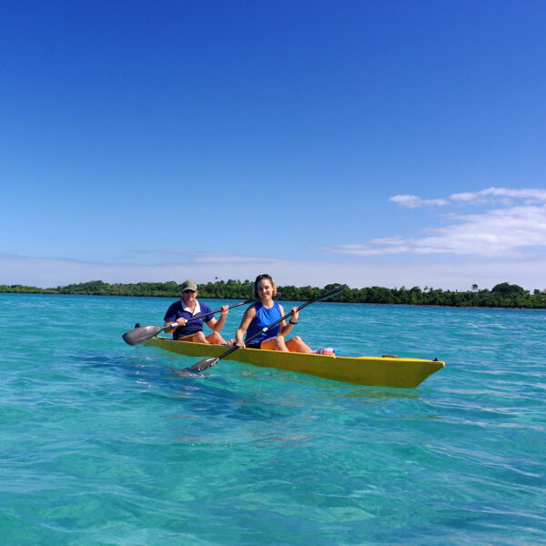 Guests in a yellow kayak on the blue waters and land in the background