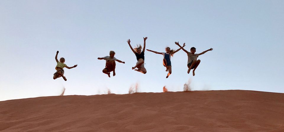 Kids jump for joy from the top of a sand dune