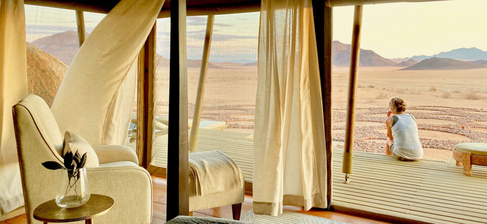 A women sits on her deck in front of her tented suite at Boulders Camp staring across the desert plains to the mountains beyond.